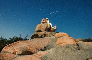 man standing on a peak watching a meteor