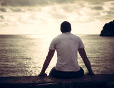 man sitting on boardwalk overlooking ocean