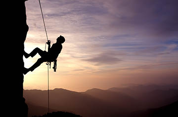 Person scaling rock at sunrise