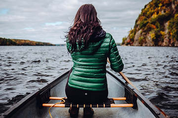 person rowing canoe in open ocean, cliffs behind