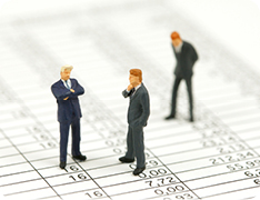 three toy businessmen atop printed spreadsheet