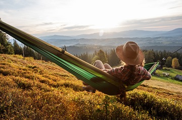 person wearing sun hat lounging in hammock to admire sunny view