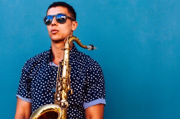 holding saxophone in front of bright blue wall