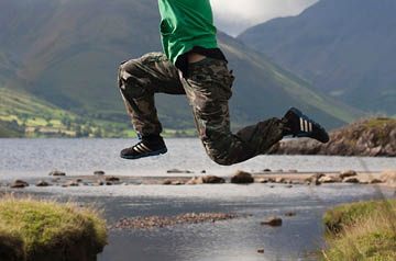 jumping over small waterway in meadow, mountains behind
