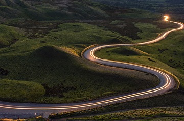 Arial view of two lane road weaving through hills with blurred headlights