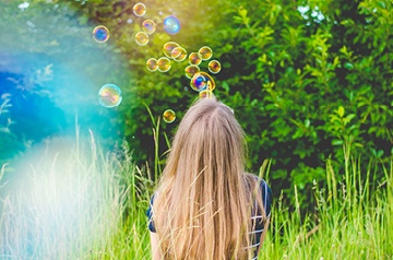 A person with long hair blowing bubbles in a field