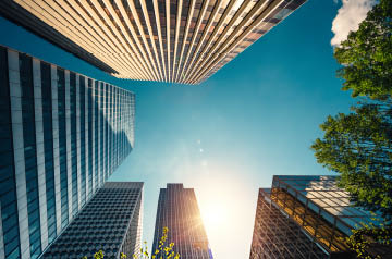 Looking up at a blue sky while surrounded by glass paneled skyscrapers