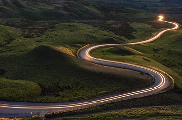 Blurred headlights on two lane road in hills at twilight
