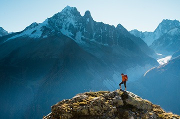 Hiker cresting mountain with mountain range in background on clear day