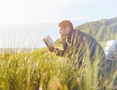 man reading book on grassy hill