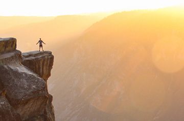 standing at cliff's edge, mountains behind