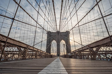 Looking up and across a bridge with struts and wires making visual pattern on blue sky