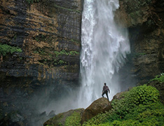 person standing on rocks in front of tall waterfall