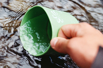 hand scooping river water with mug