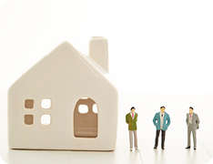 Toy businesspeople standing next to toy house