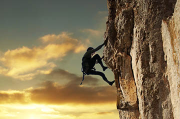 Person scaling a cliff at sunrise