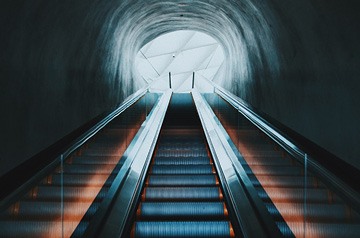 pair of escalators leading from a dark space up to a room full of natural daylight