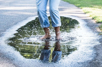 A person in jeans jumping in a puddle