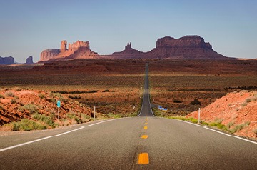 Looking down a two-lane road towards distant mesa formations