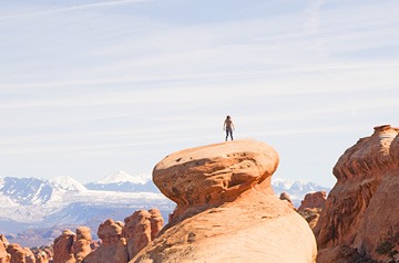 standing on tall rock formation, desert hills behind
