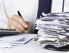 hand signing a paper next to a stack of documents