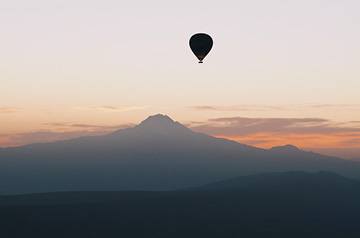 hot air balloon floating near a mountain peak at sunrise